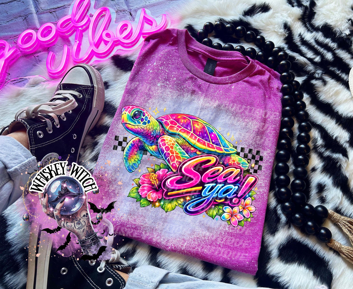 A Berry pink t-shirt with bleach white effect a colorful graphic of a sea turtle, flowers, and the words "Sea Ya!". The shirt has a bleached, distressed look. The design features vibrant colors and a playful font.