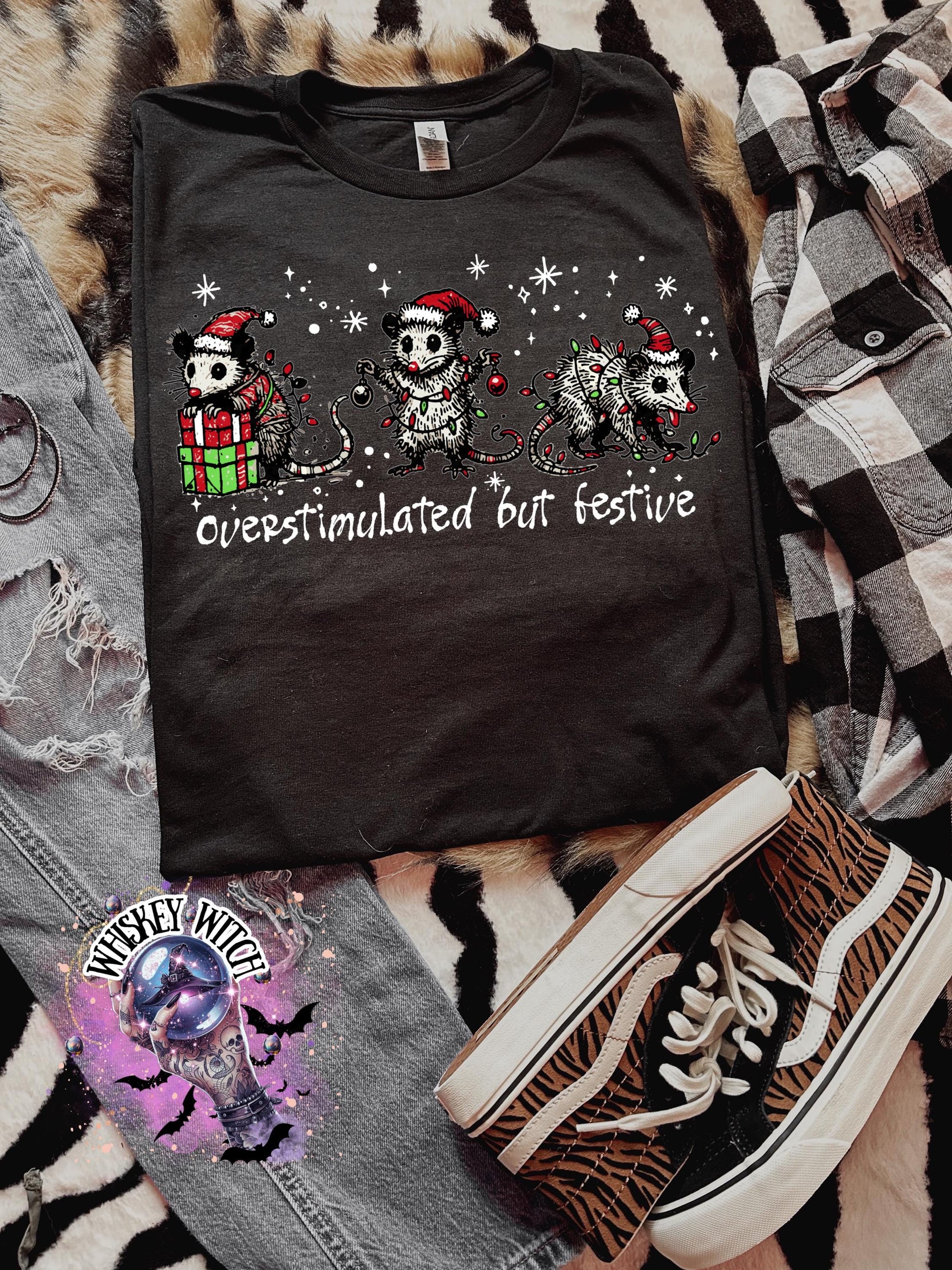 Black unisex sweatshirt with ‘Overstimulated but Festive’ skeleton Christmas graphic, snowflake accents, modeled indoors