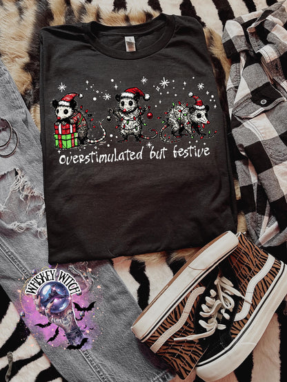 Black unisex sweatshirt with ‘Overstimulated but Festive’ skeleton Christmas graphic, snowflake accents, modeled indoors