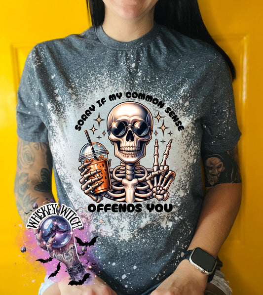 A bleached splattered gray t-shirt with a graphic of a skeleton wearing sunglasses and holding a drink. The text on the shirt reads "SORRY IF MY COMMON SENSE OFFENDS YOU."