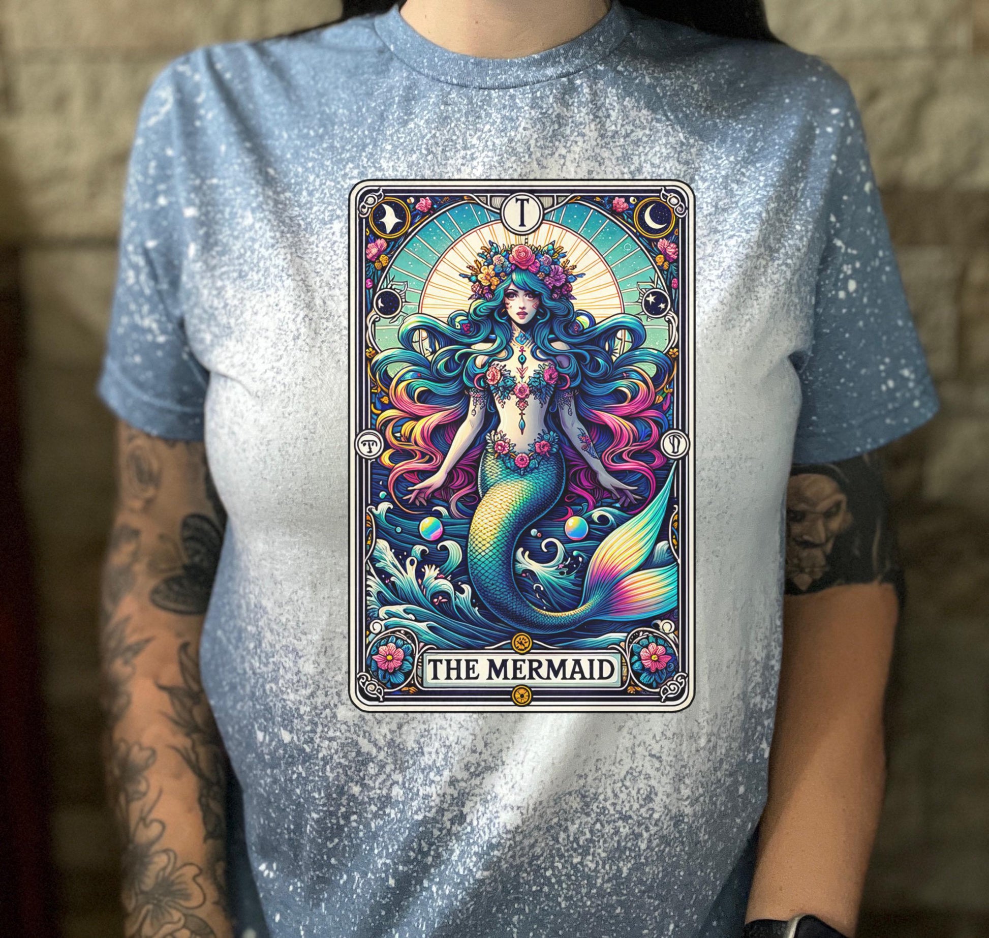 Mystical mermaid tarot card graphic centered on a indigo  bleach-dyed shirt, photographed with neon pink sign and cozy background props.