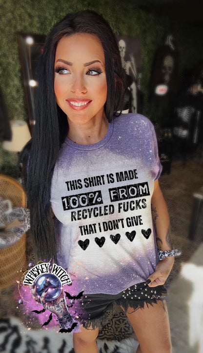 purple  t-shirt with the text "THIS SHIRT IS MADE 100% FROM RECYCLED FUCKS THAT I DON'T GIVE" in black. The shirt has a bleached effect and four black heart graphics. A pair of black and white checkered sneakers are at the bottom.