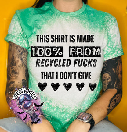 Green t-shirt with the text "THIS SHIRT IS MADE 100% FROM RECYCLED FUCKS THAT I DON'T GIVE" in black. The shirt has a bleached effect and four black heart graphics. A pair of black and white checkered sneakers are at the bottom.