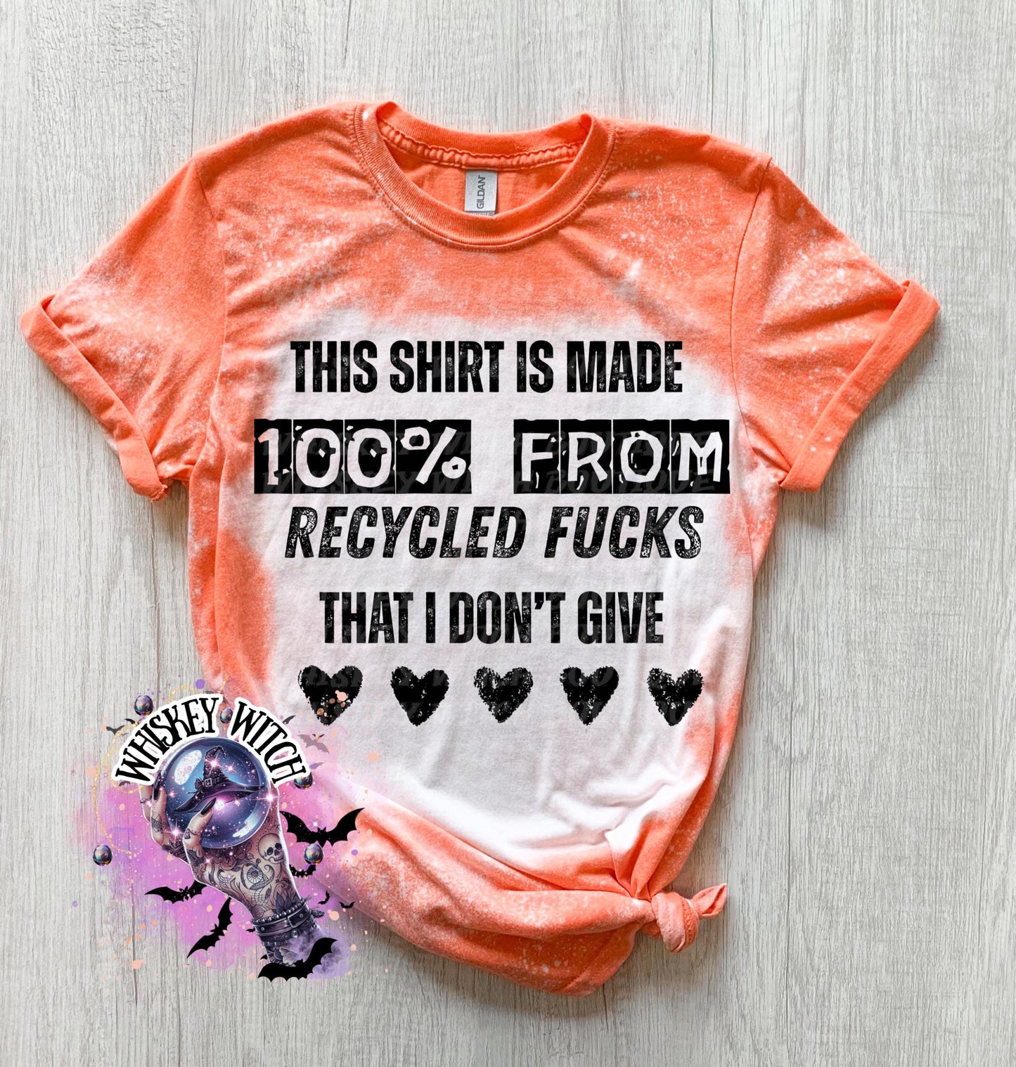 Orange t-shirt with the text "THIS SHIRT IS MADE 100% FROM RECYCLED FUCKS THAT I DON'T GIVE" in black. The shirt has a bleached effect and four black heart graphics. A pair of black and white checkered sneakers are at the bottom.
