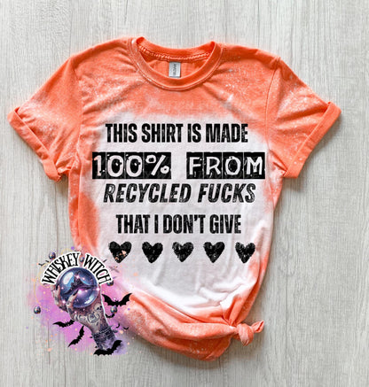 Orange t-shirt with the text "THIS SHIRT IS MADE 100% FROM RECYCLED FUCKS THAT I DON'T GIVE" in black. The shirt has a bleached effect and four black heart graphics. A pair of black and white checkered sneakers are at the bottom.