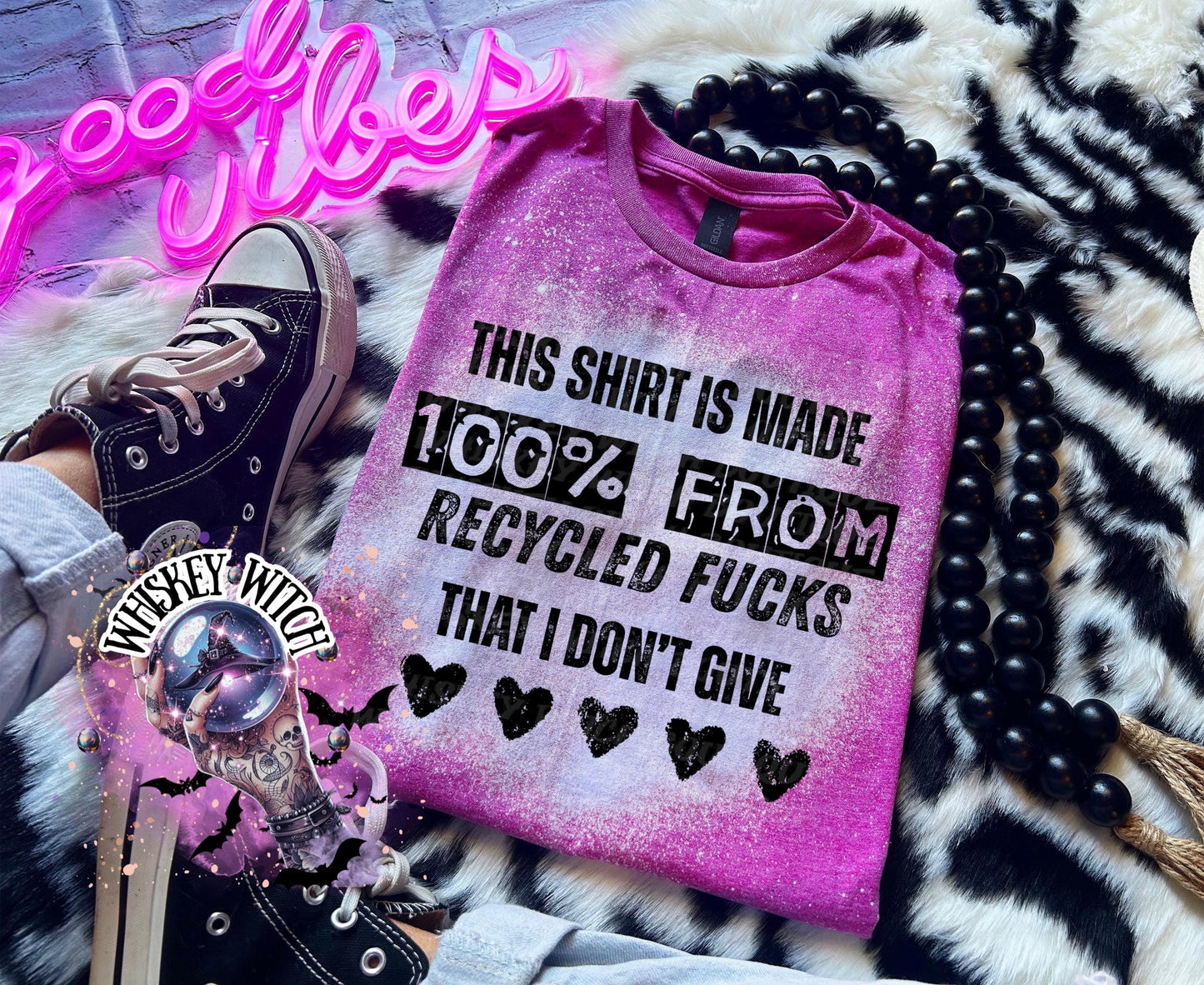 A Berry pink t-shirt with the text "THIS SHIRT IS MADE 100% FROM RECYCLED FUCKS THAT I DON'T GIVE" in black lettering. The shirt has a bleached effect and four black heart graphics. A pair of black high-top sneakers is visible.