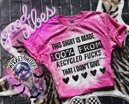 Pink t-shirt with the text "THIS SHIRT IS MADE 100% FROM RECYCLED FUCKS THAT I DON'T GIVE" in black. The shirt has a bleached effect and four black heart graphics. A pair of black and white checkered sneakers are at the bottom.