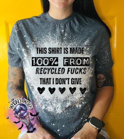 Gray t-shirt with the text "THIS SHIRT IS MADE 100% FROM RECYCLED FUCKS THAT I DON'T GIVE" in black. The shirt has a bleached effect and four black heart graphics. A pair of black and white checkered sneakers are at the bottom.