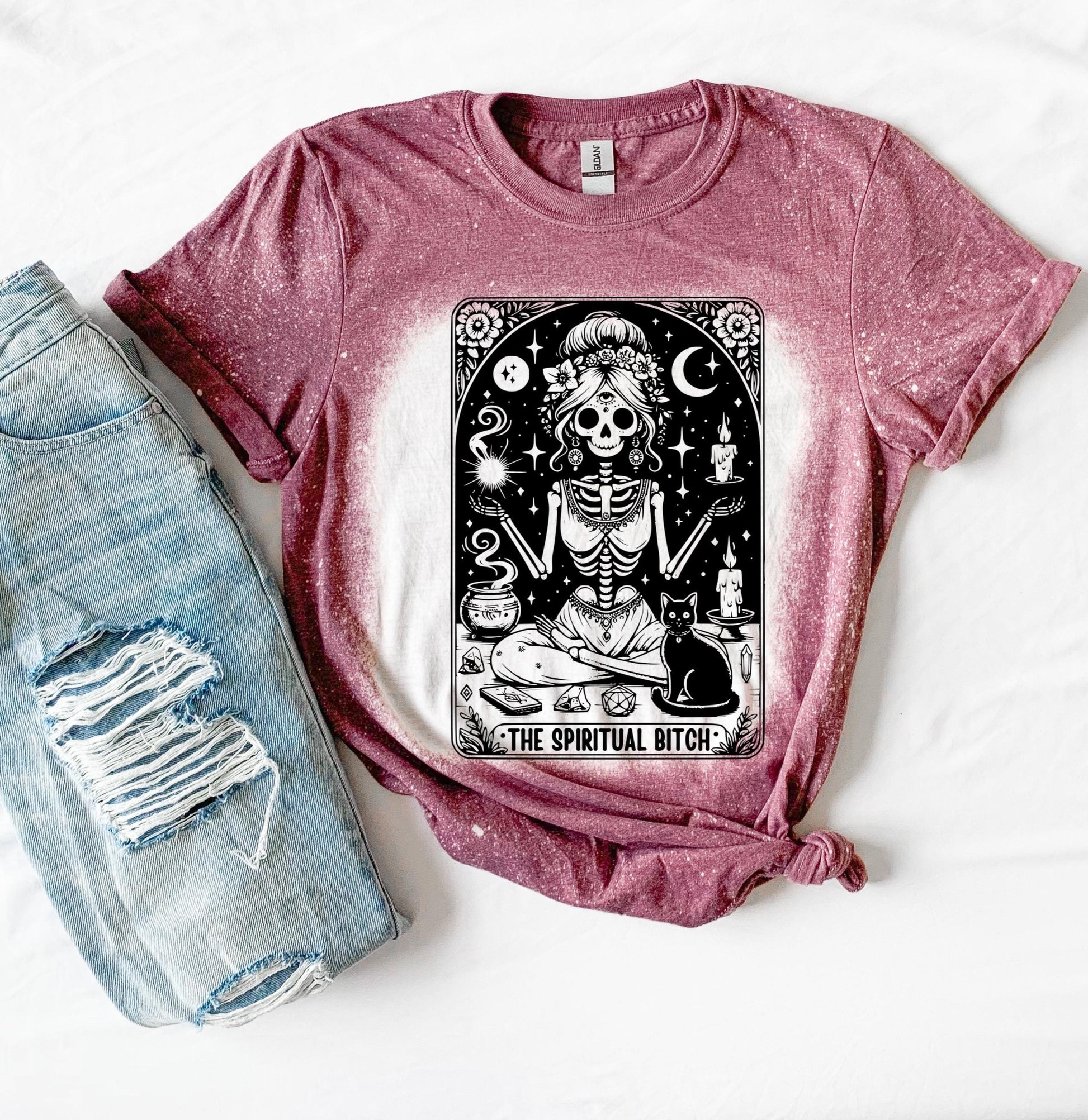 A bleached maroon t-shirt with a black and white illustration of a skeleton woman with a cat and the text "The Spiritual Bitch".