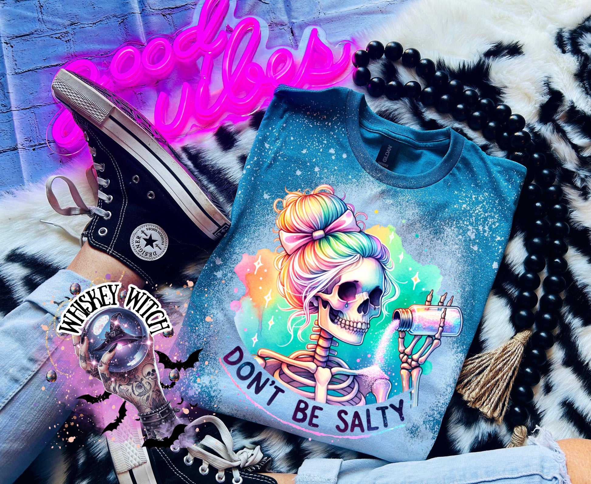 A Galapagos blue t-shirt with a bleached effect featuring a skeleton with rainbow hair pouring salt from a shaker. The text "Don't Be Salty" is printed on the shirt