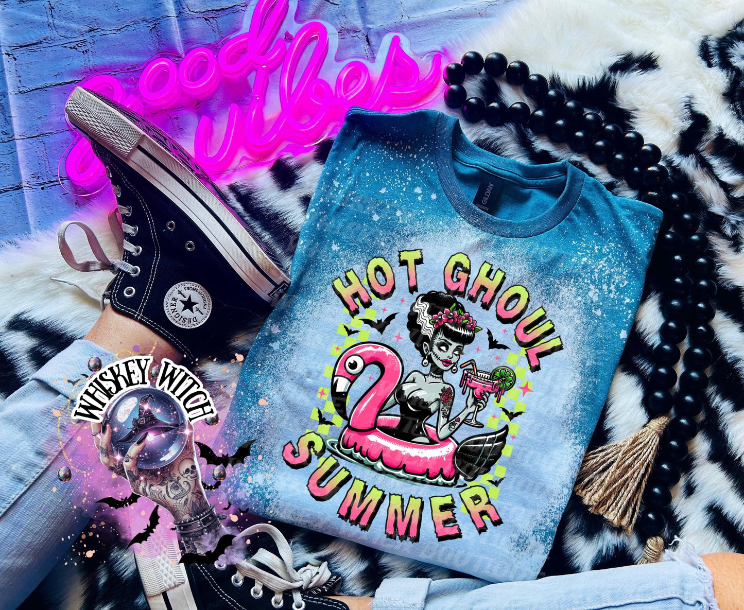 A Galapagos blue and bleach splattered effect  t-shirt with a graphic of a zombie woman in a flamingo pool float, holding a cocktail. The text "Hot Ghoul Summer" is printed on the shirt.