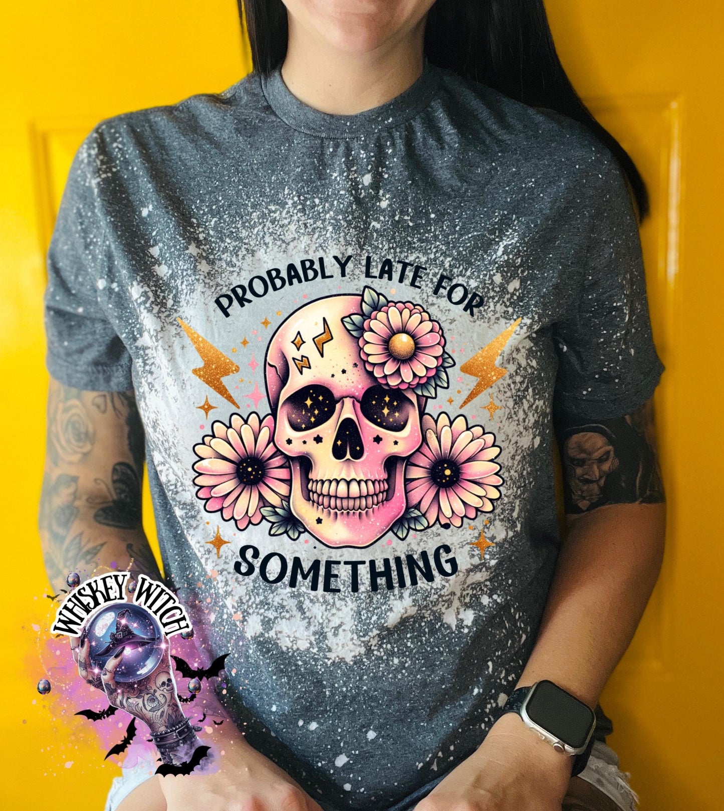 A grey t-shirt with a bleached effect featuring a skull with flowers and the text "Probably Late For Something" in gold glitter.