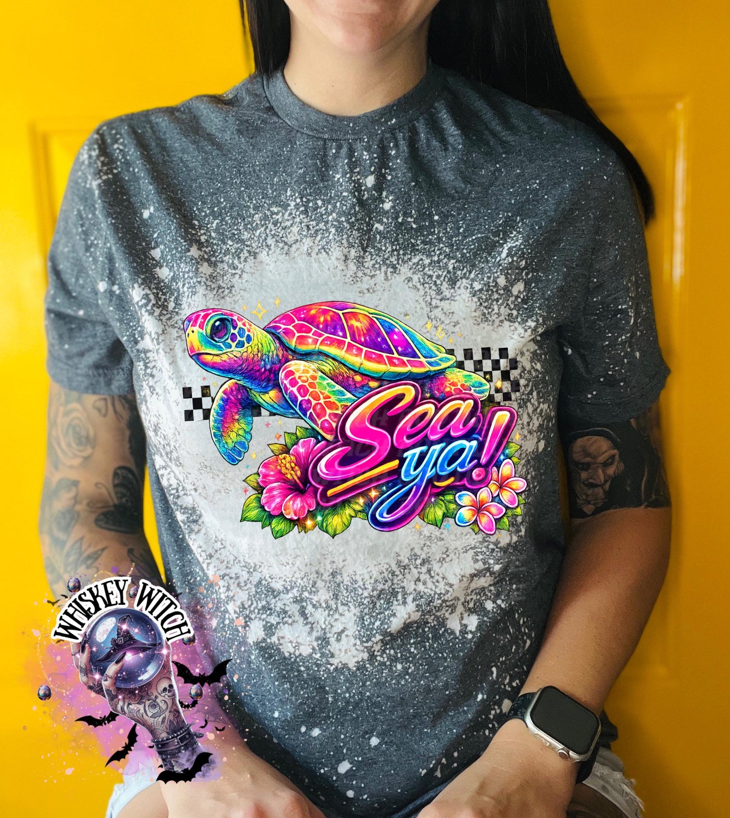A grey t-shirt with bleach white effect a colorful graphic of a sea turtle, flowers, and the words "Sea Ya!". The shirt has a bleached, distressed look. The design features vibrant colors and a playful font.
