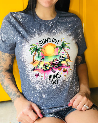 A navy blue  t-shirt with a graphic of a skeleton relaxing on a beach with palm trees and the text "Sun's Out Buns Out." The shirt has a bleached effect.