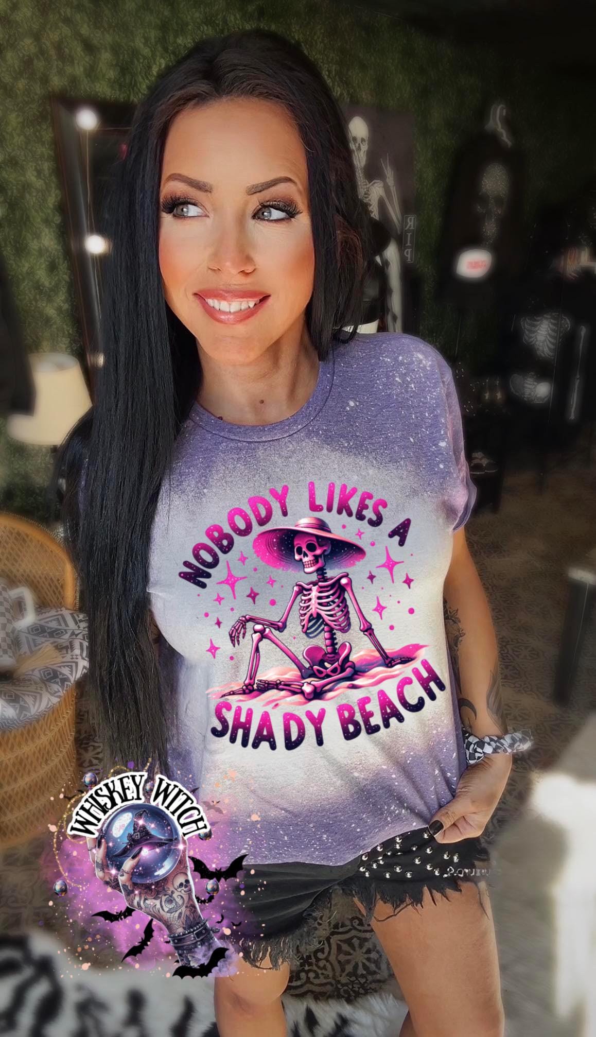 A purple  t-shirt with a bleached design featuring a skeleton wearing a hat, the text "Nobody Likes a Shady Beach," and star graphics. The shirt is paired with black and white checkered sneakers.