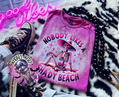 A Berry  pink t-shirt with a bleached design featuring a skeleton wearing a hat, the text "Nobody Likes a Shady Beach," and star graphics. The shirt is paired with black and white checkered sneakers.