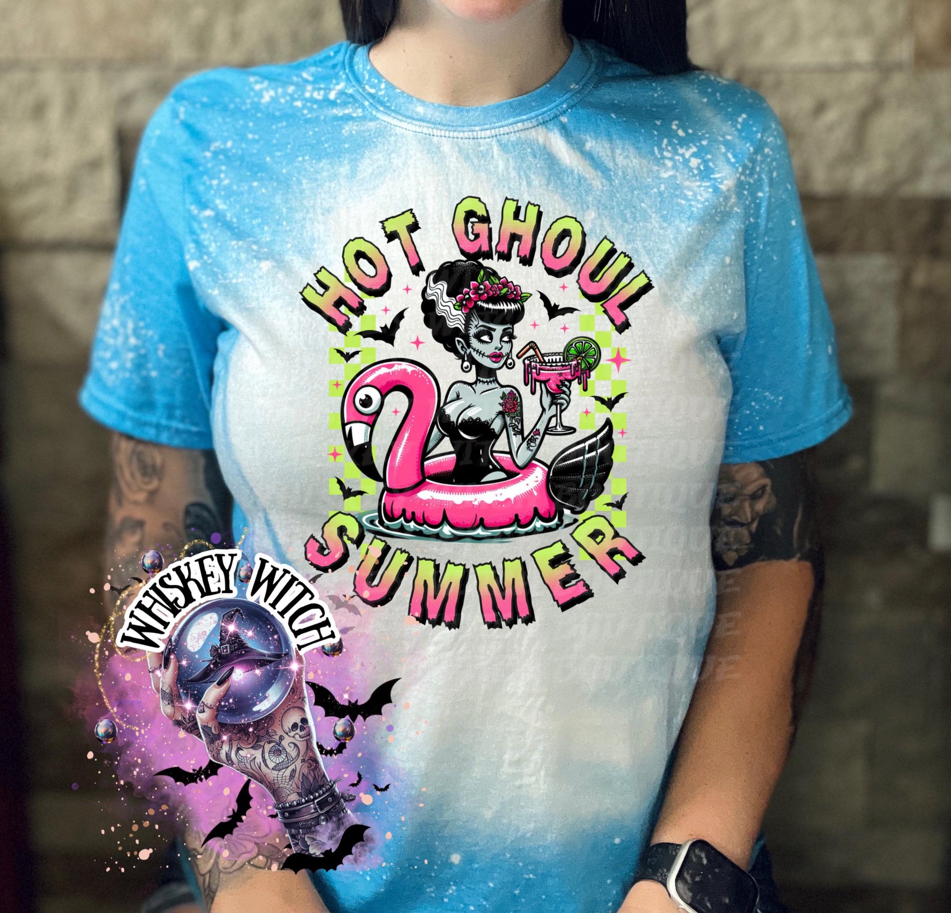 A sapphire blue  and bleach splattered effect  t-shirt with a graphic of a zombie woman in a flamingo pool float, holding a cocktail. The text "Hot Ghoul Summer" is printed on the shirt.