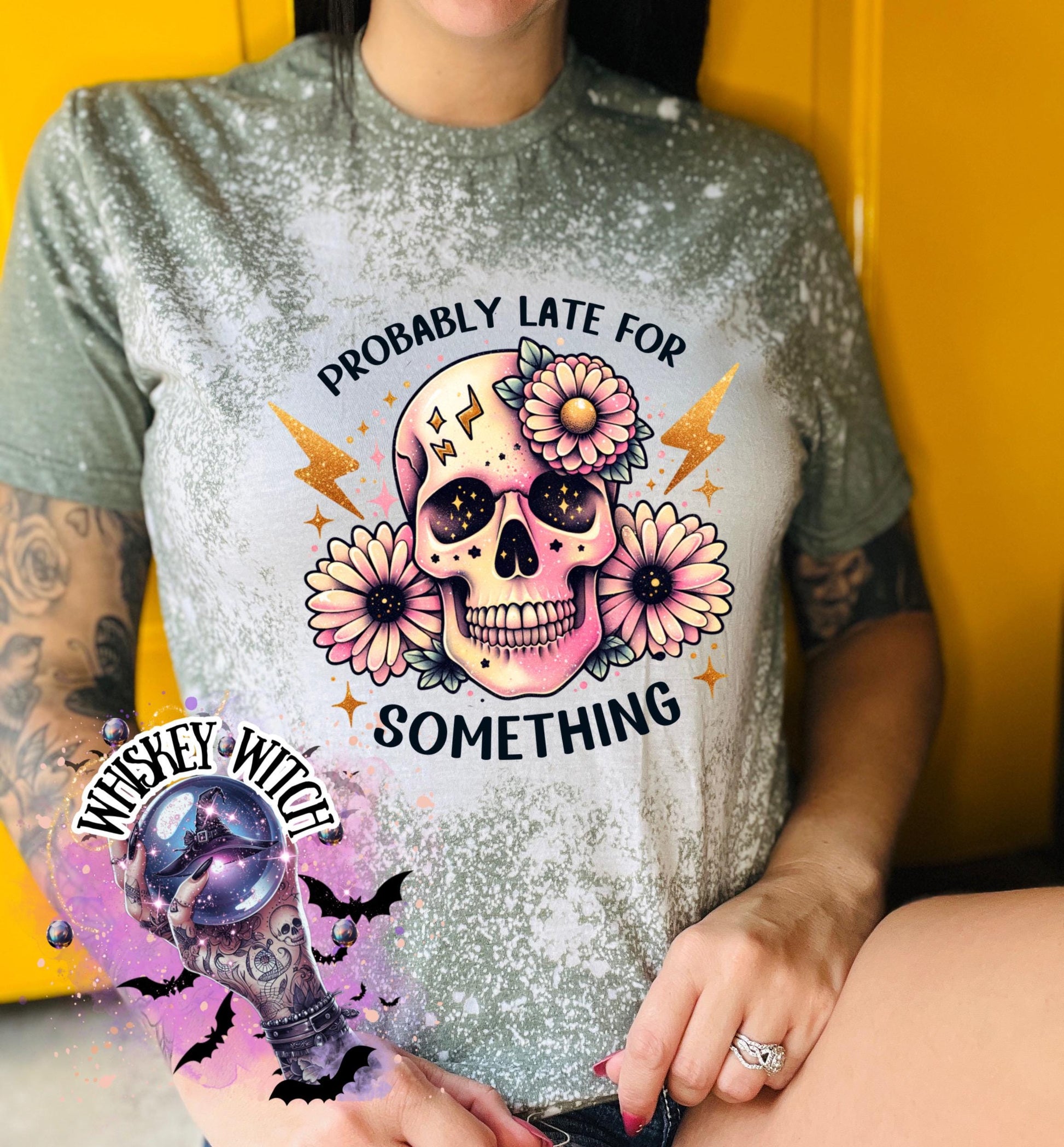 A military green  t-shirt with a bleached effect featuring a skull with flowers and the text "Probably Late For Something" in gold glitter.
