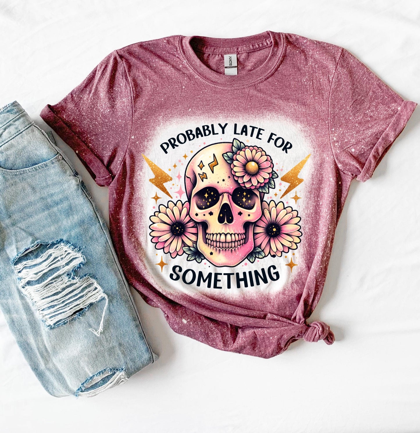 A maroon t-shirt with a bleached effect featuring a skull with flowers and the text "Probably Late For Something" in gold glitter.