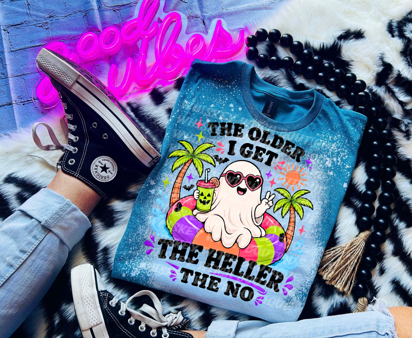 A blue t-shirt with a graphic of a ghost wearing sunglasses and a drink, with the text "The Older I Get The Heller The No". The shirt is paired with black Converse sneakers.