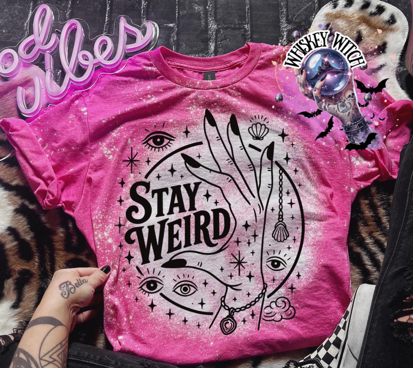 Handmade bleached styles shirt. Close-up of witchy Stay Weird shirt design with celestial artwork, mystical hands, stars, and bold black text