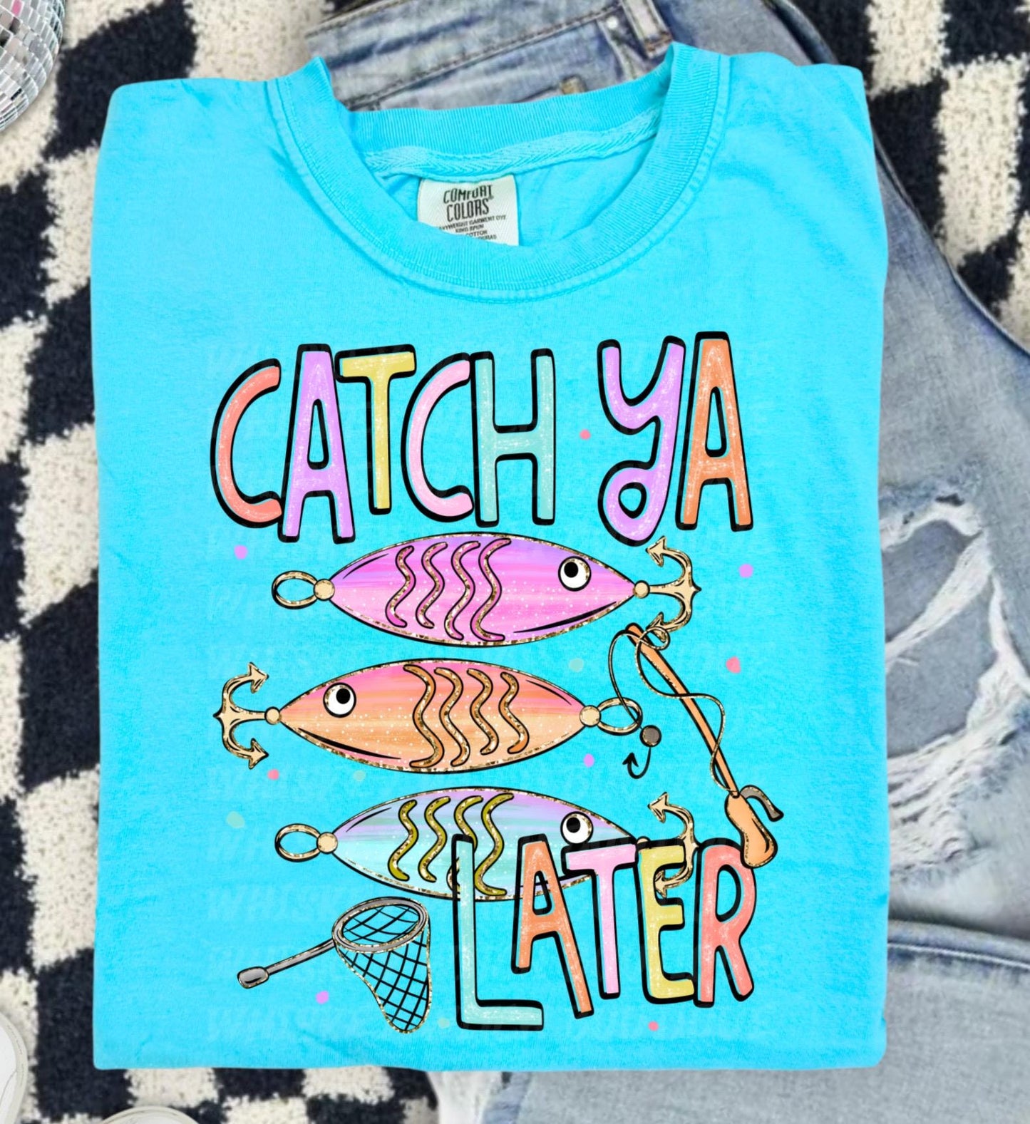 Cute lake day graphic tee with Catch Ya Later text, fishing lures, and a small fishing net design.