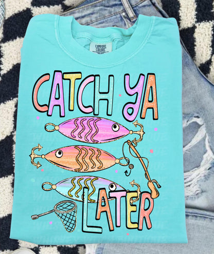 Cute lake day graphic tee with Catch Ya Later text, fishing lures, and a small fishing net design.