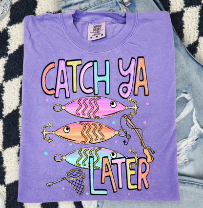 Cute lake day graphic tee with Catch Ya Later text, fishing lures, and a small fishing net design.
