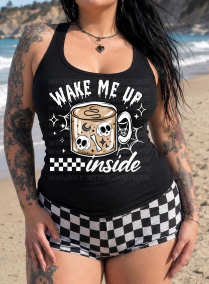 Black tank top with spooky coffee skull mug graphic and bold white Wake Me Up lettering, styled on a beach with checkered shorts